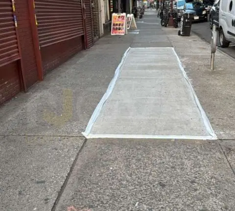 Rectangular sidewalk repair curing on a busy commercial street